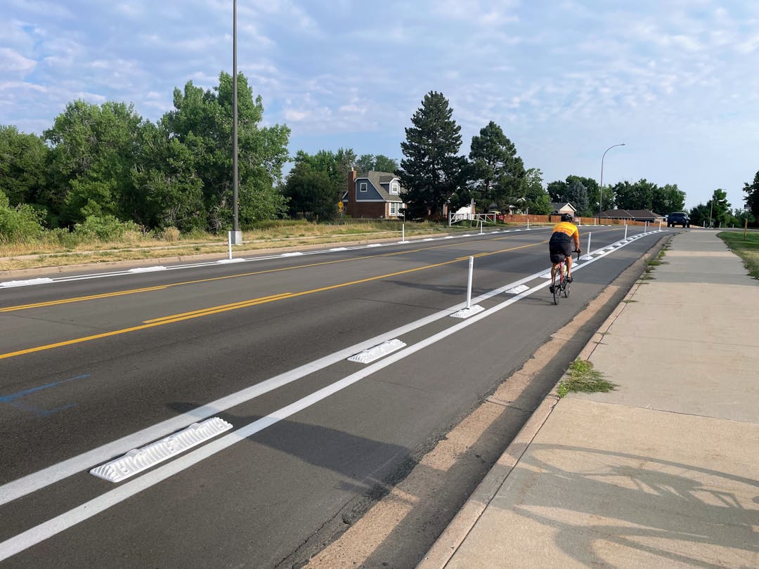 A bicyclist riding in a bike lane separated from the road with plastic curbs and posts