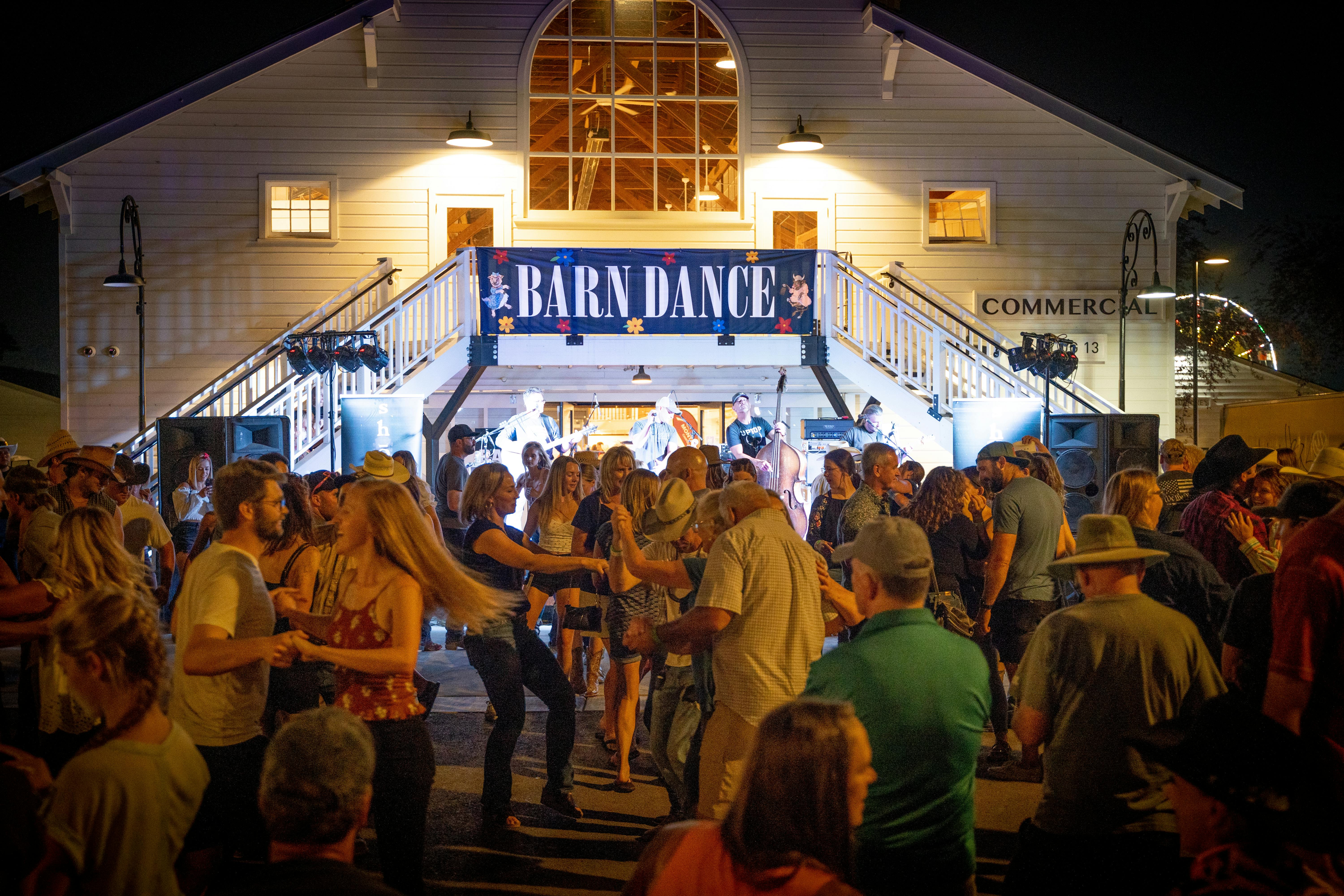 A photo of a lively barn dance in front of the Commercial Building at night. 