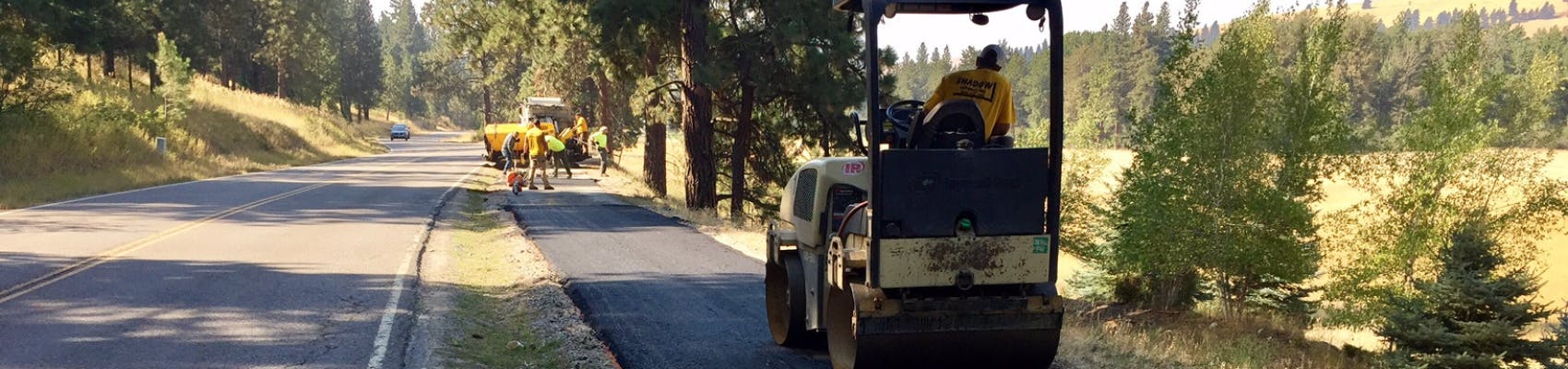 Public Works road crew working on trail alongside rural County road on summer day.