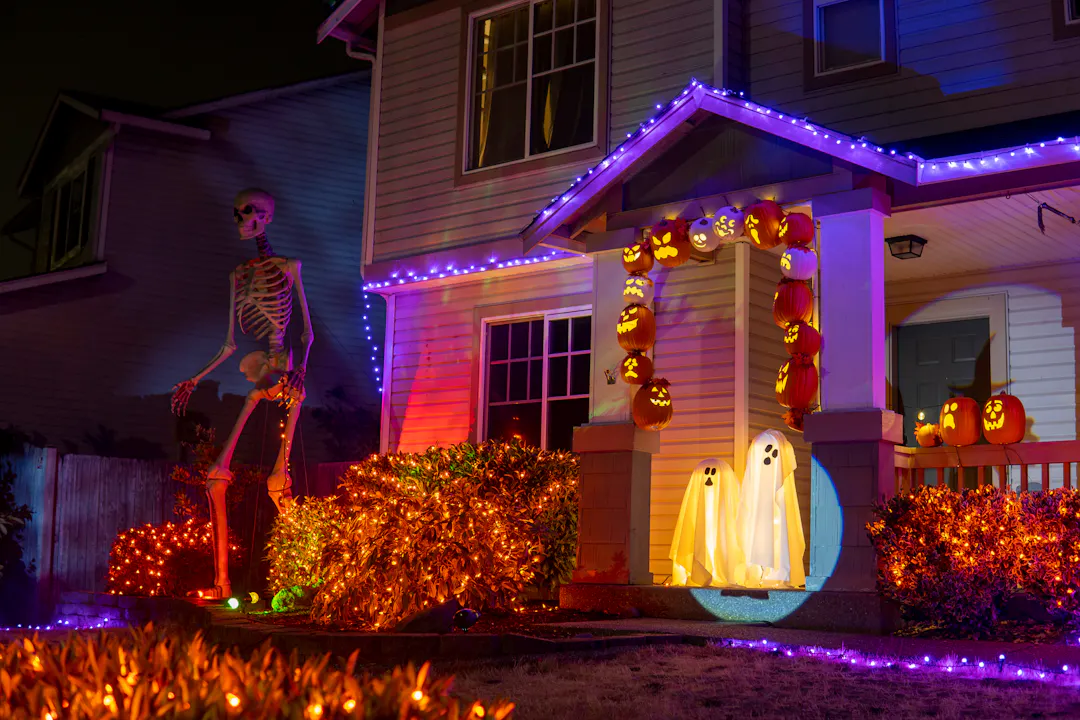 A home decorated for Halloween with orange lights, giant skeleton, ghosts and several jack-o-lanterns on the porch.