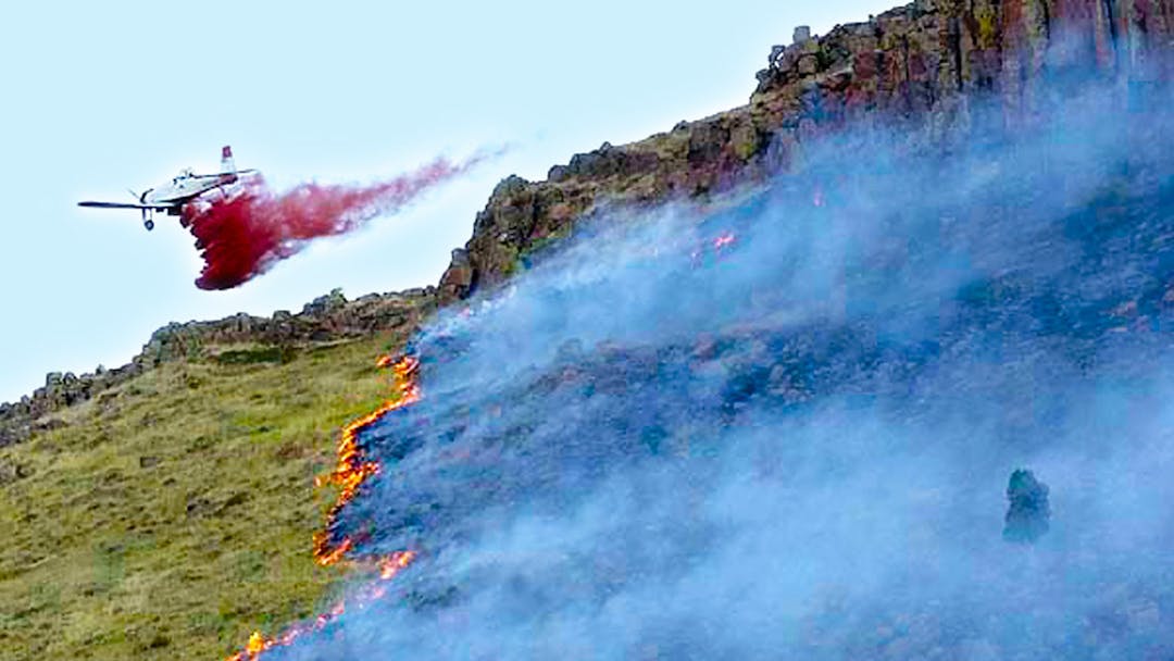 Plane drops retardant on a hillside that's burning during a wildfire.