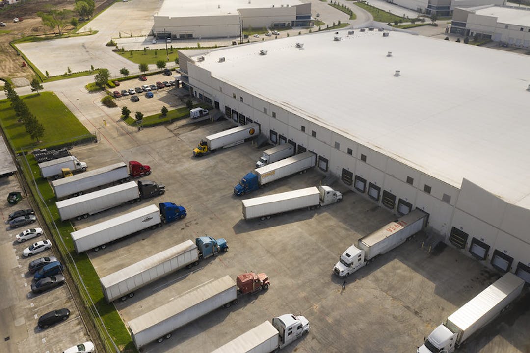 This image shows a large warehouse with roughly a dozen semi trucks loading or unloading shipments.
