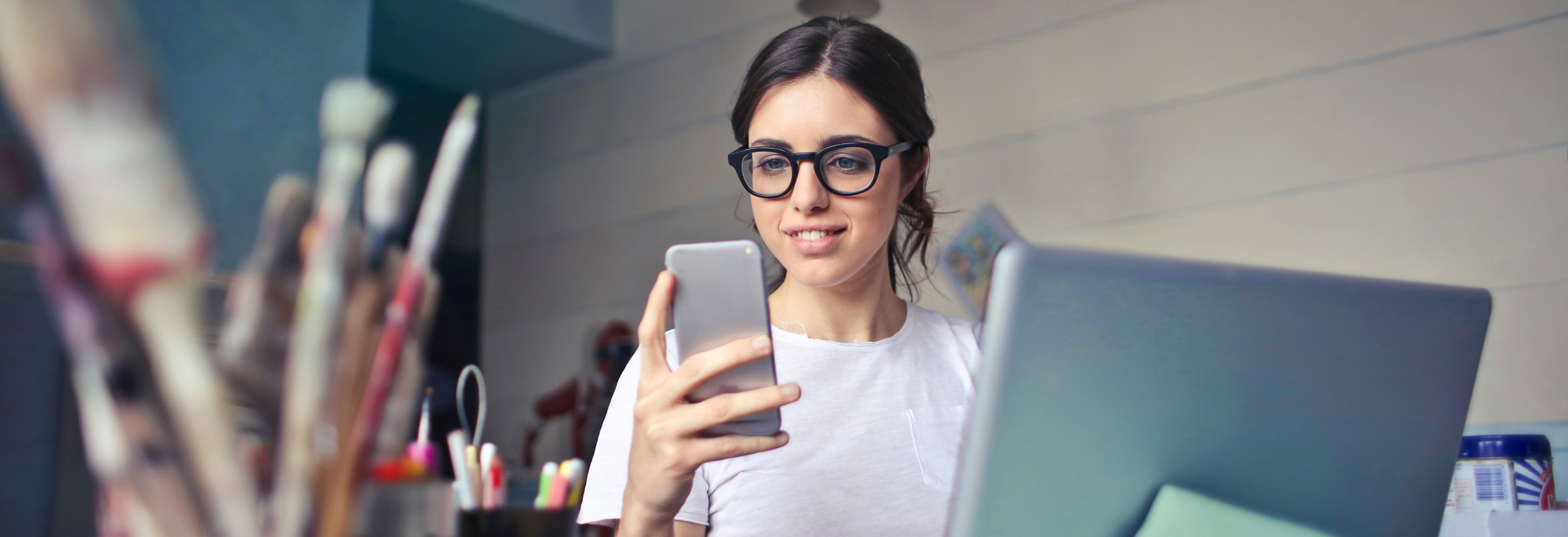 woman sitting with a laptop while looking at a cell phone