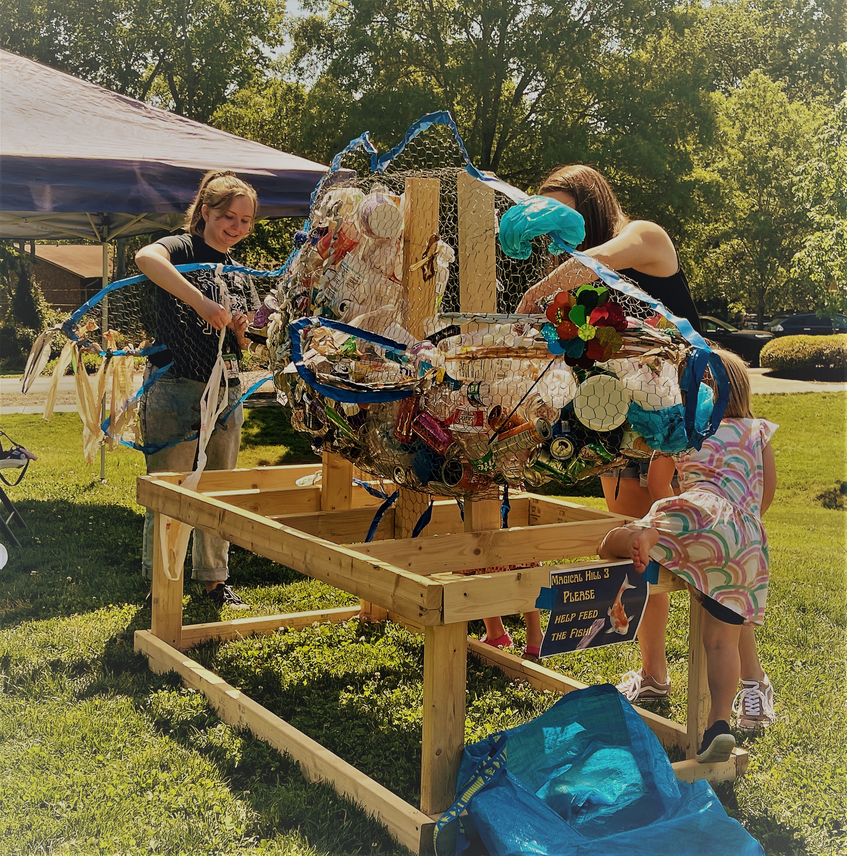 Photo of people putting trash inside a metal framed fish.