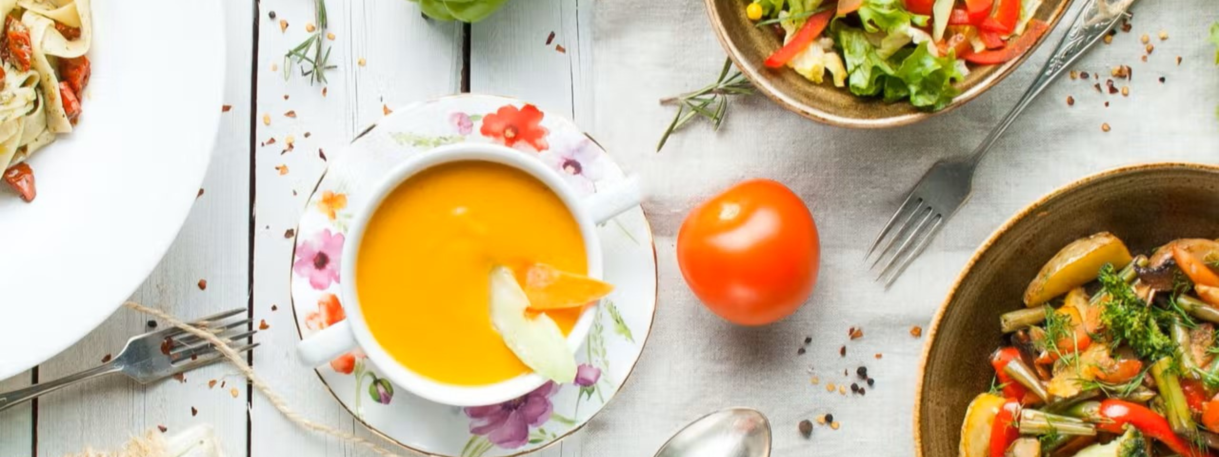 Orange soup, salads, silverware, a tomato and redpepper flakes