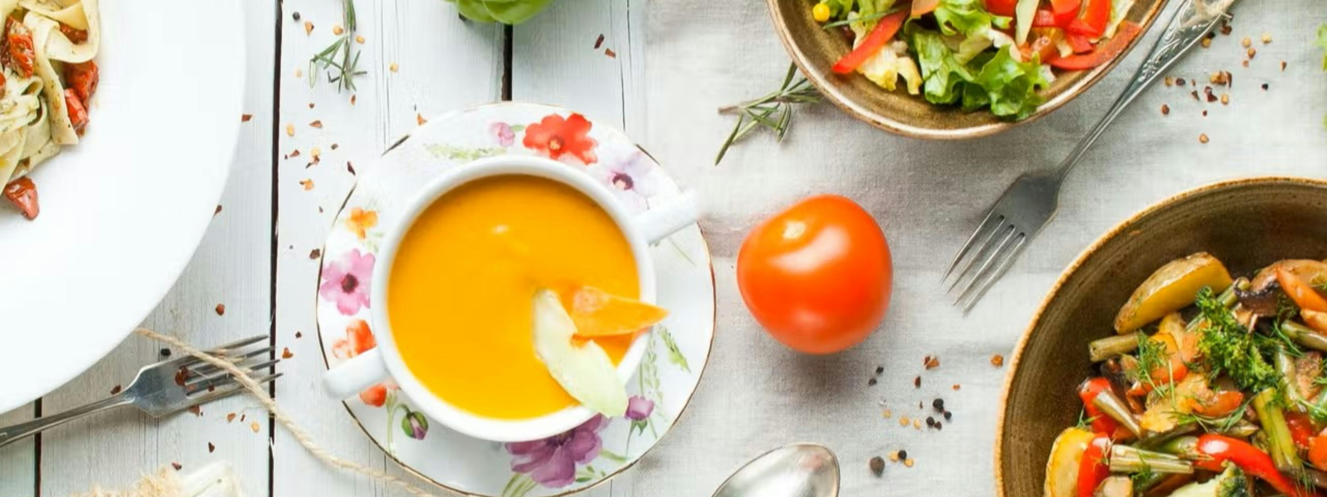 Orange soup, salads, silverware, a tomato and redpepper flakes