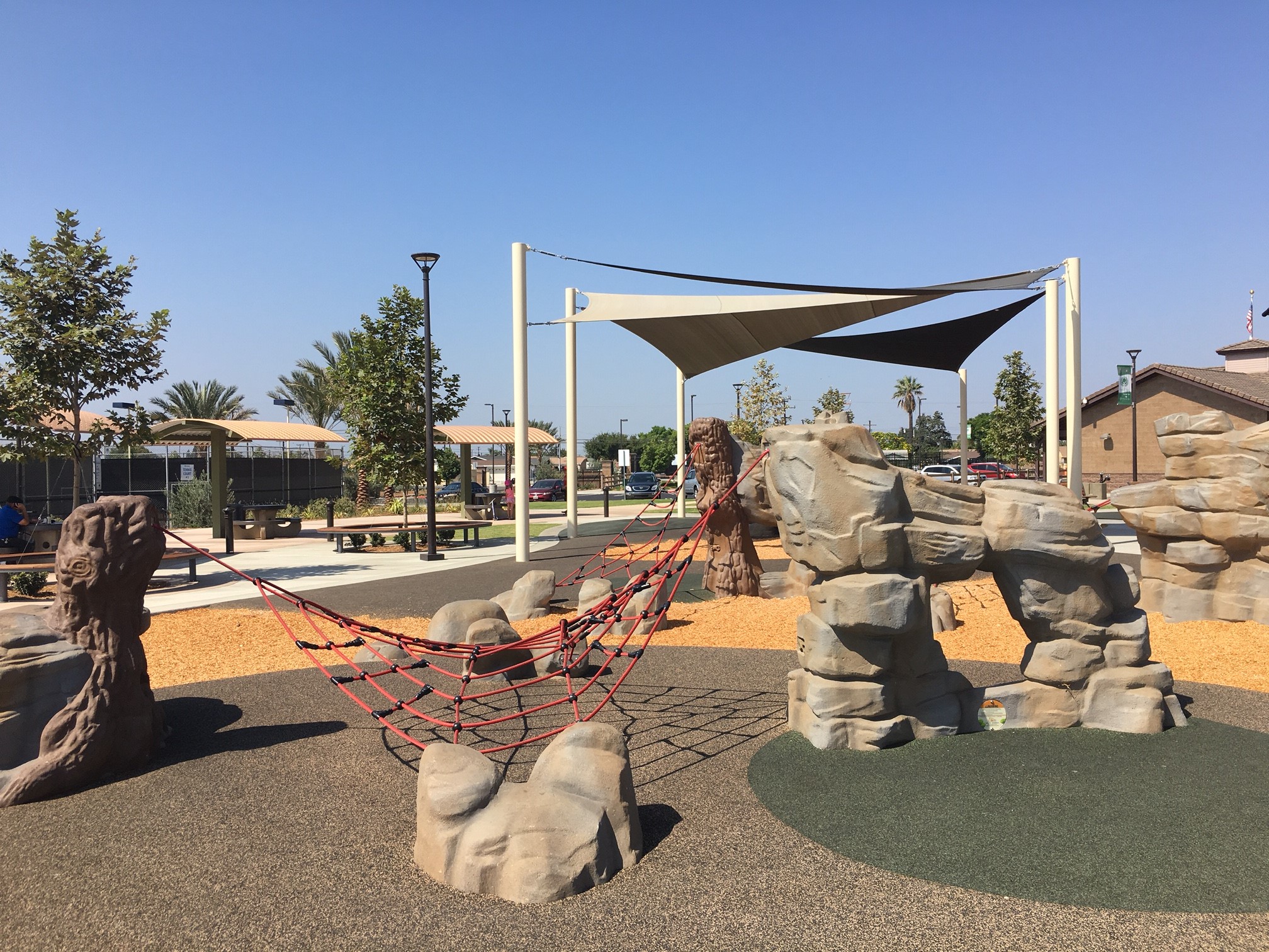natural playground features including boulders, nets, and shade structures
