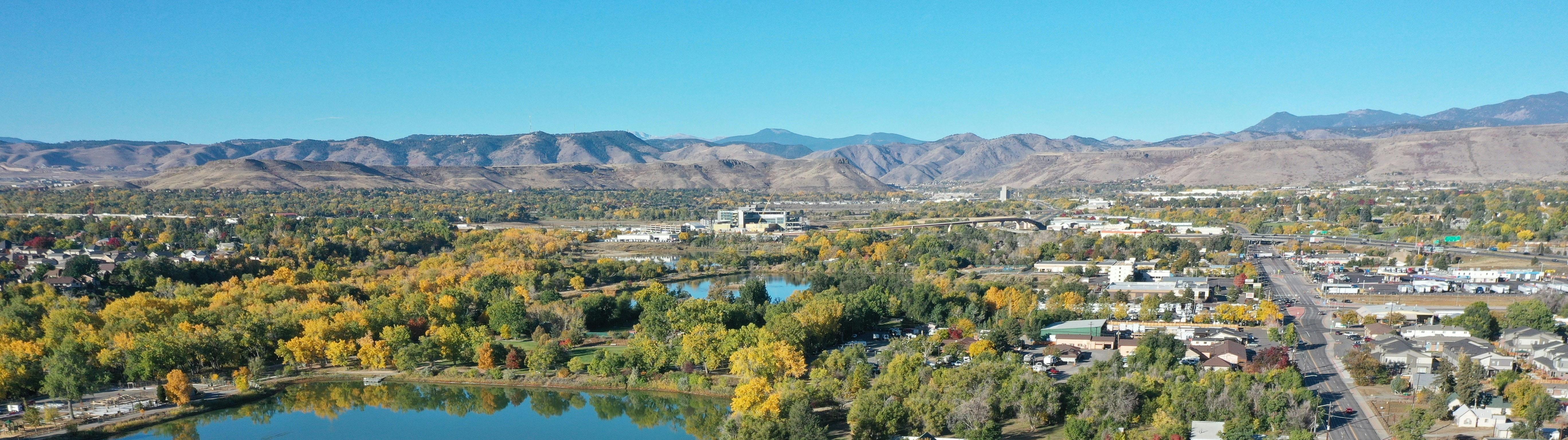 Aerial image of Wheat Ridge  with trees and buildings in the foreground and the Front Range mountains in the background