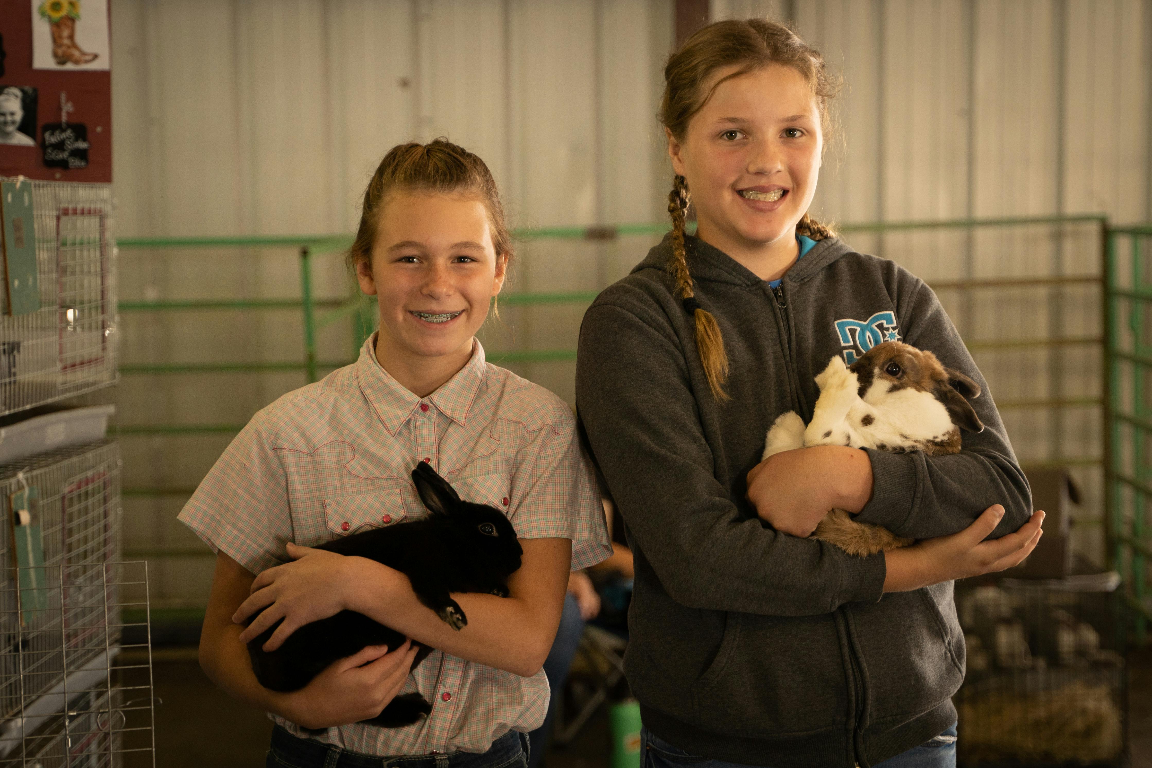 Two girls in 4-H stand with their bunnies in their arms.