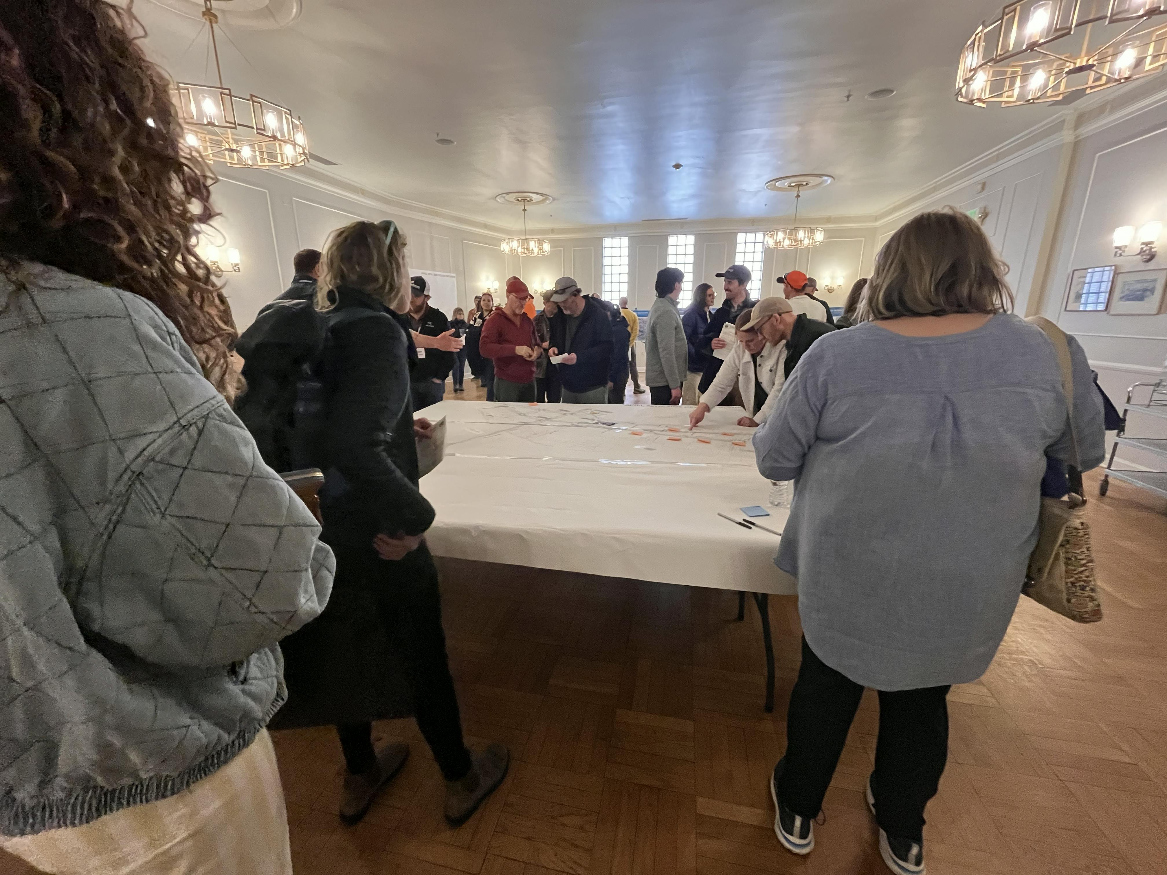 Open House 2 - People stand around a table with a map. One person points to the map.png
