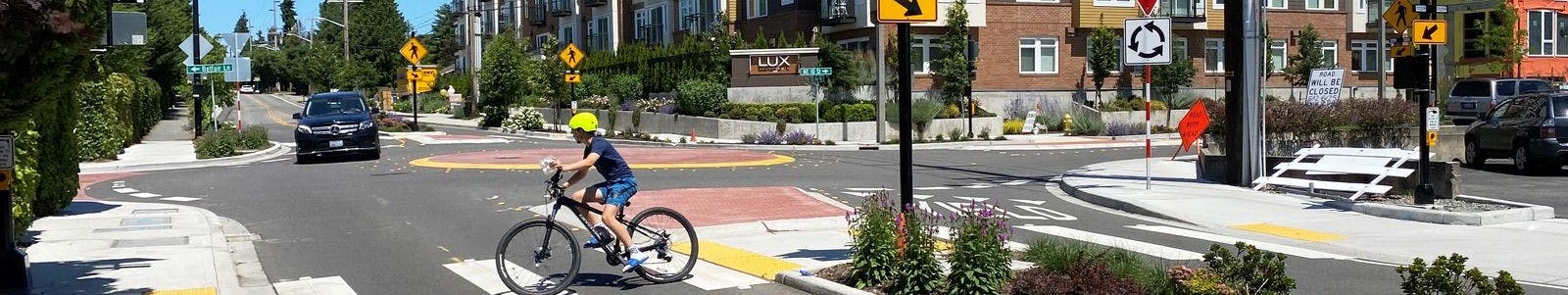 A teenager bikes across a signed crosswalk next to a roundabout in Downtown Bellevue