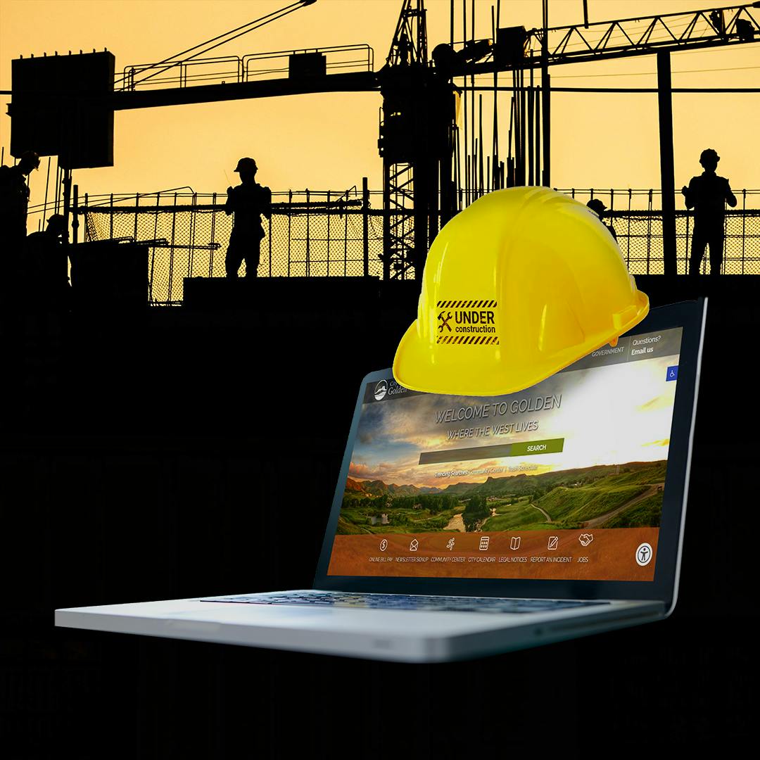 A construction hard hat is propped on a laptop computer open to the City of Golden website.