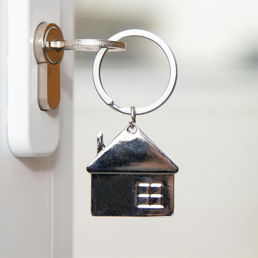 A key on a house-shaped keychain sits in a door lock