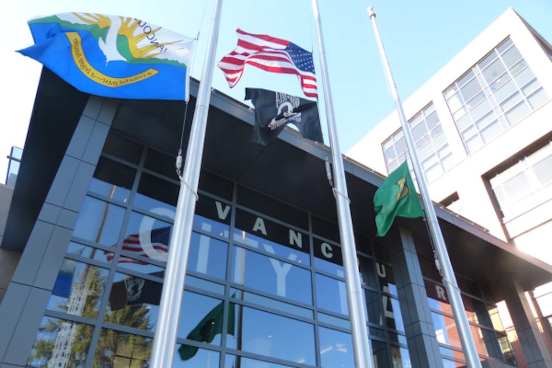 This photo shows flags flying in front of the front entrance to Vancouver City Hall.