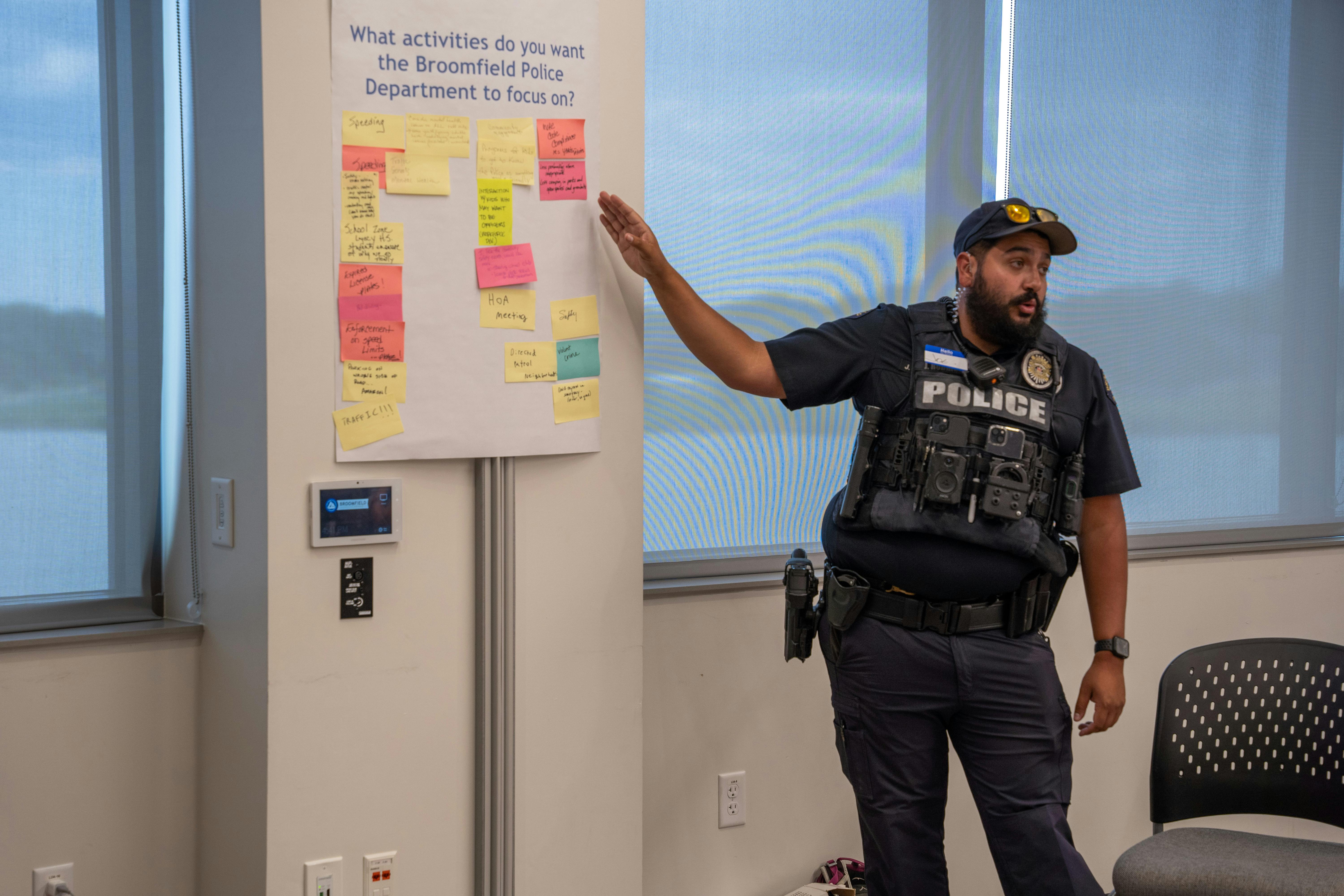 Officer points to sticky notes on a poster as he reports back to the large group on what he heard