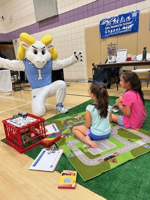 Ramses the UNC Mascot talks to two kids who are playing on a small green carpet 