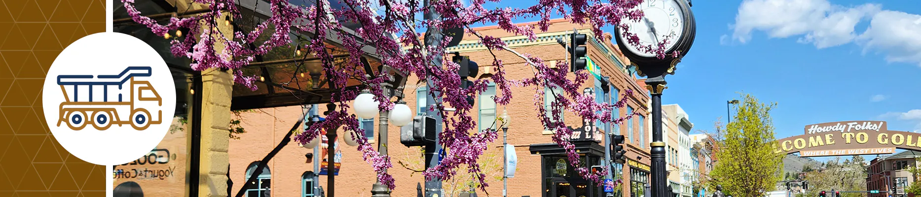 Downtown Golden in the spring with tree blossoms and the clock in the foreground, and the arch in the background.