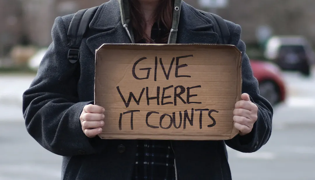 Panhandler holding a sign saying give where it counts