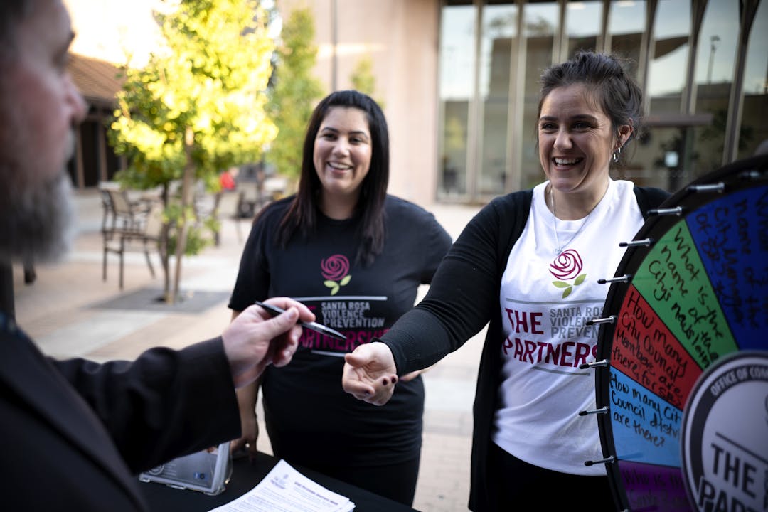 Two smiling women and a man at a community event involving free prize giveaways