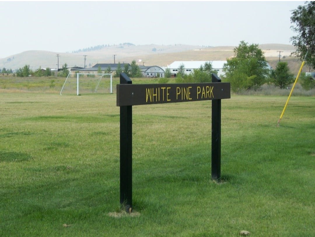 Green grass and hills in the background. White Pine Park sign.