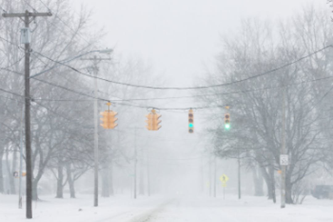 A road is covered in snow. Above the road is a traffic signal showing a green light.