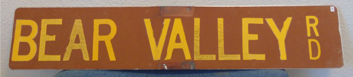 A brown street sign with yellow lettering that says Bear Valley Road