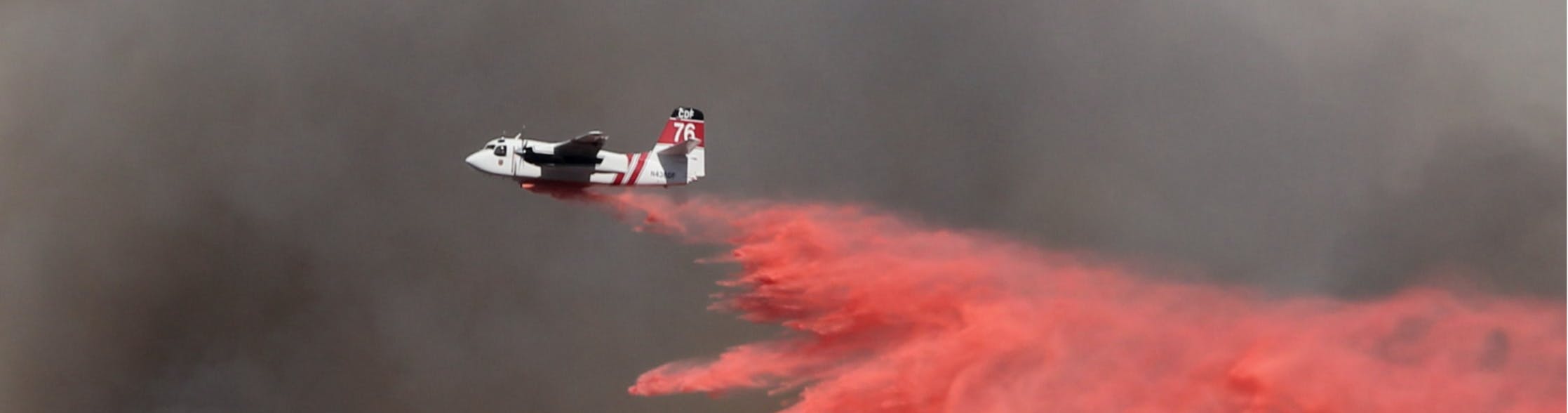 a plane dropping pink fire retardant chemicals over a wildfire