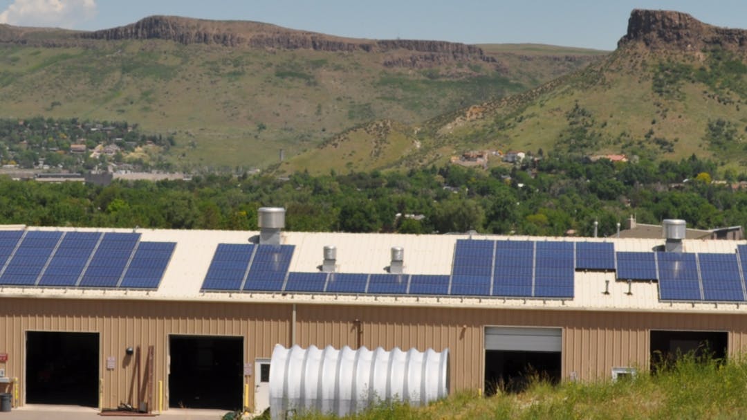 Solar panels line the roof of a warehouse with the Golden foothills rising in the background.