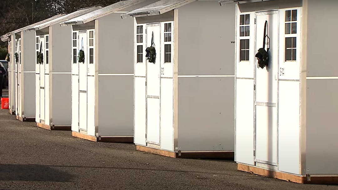 This image shows a row of pallet shelters in the City's first Safe Stay Community. The shelters are white in color.