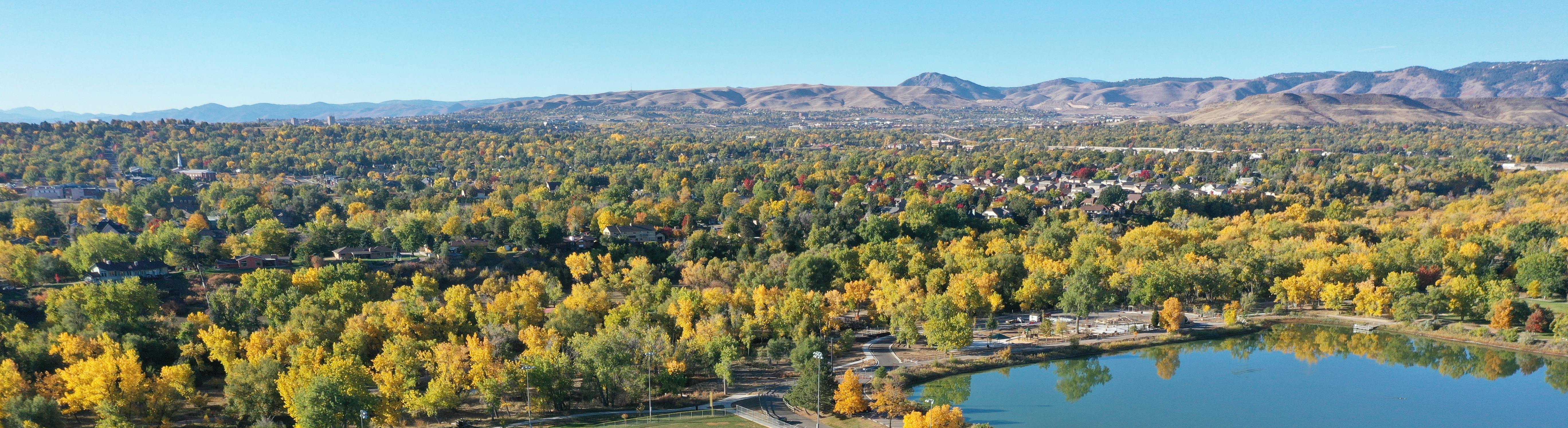 Aerial image of Wheat Ridge with trees and lake in foreground and mountains in background