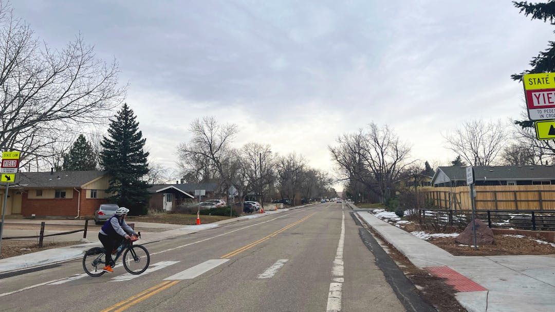 A bicyclist crosses Moorhead Avenue at the crosswalk at Bear Creek Multi-Use Path