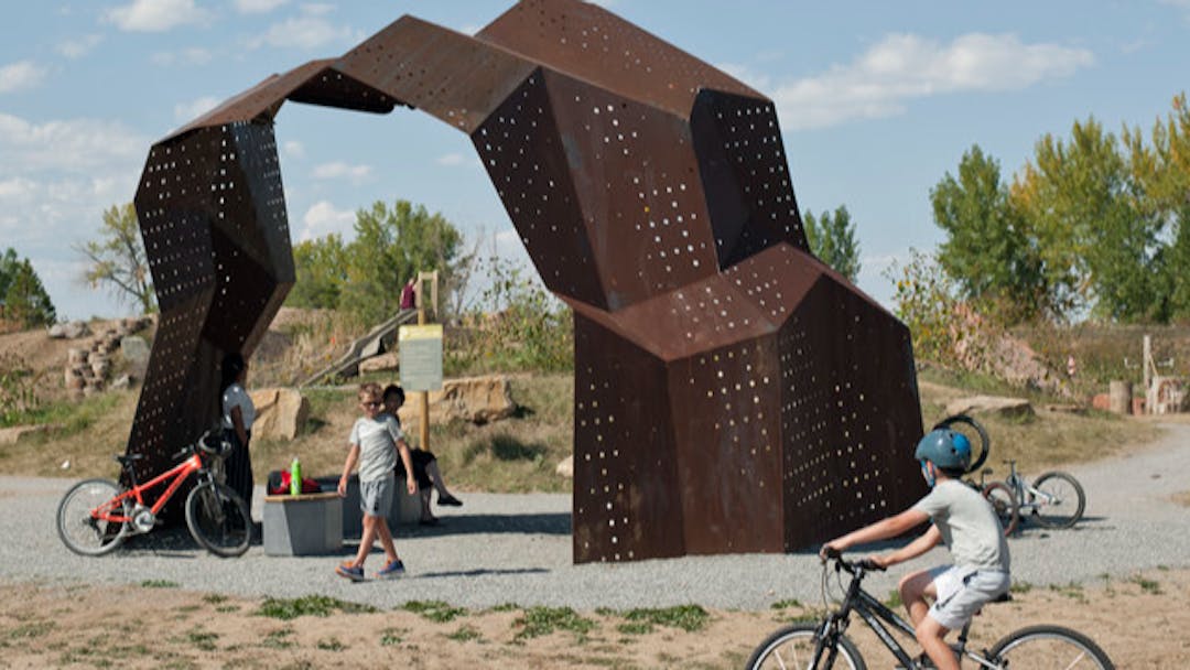 Photo of children riding bicycles under a metal art piece at McKay Lake Park