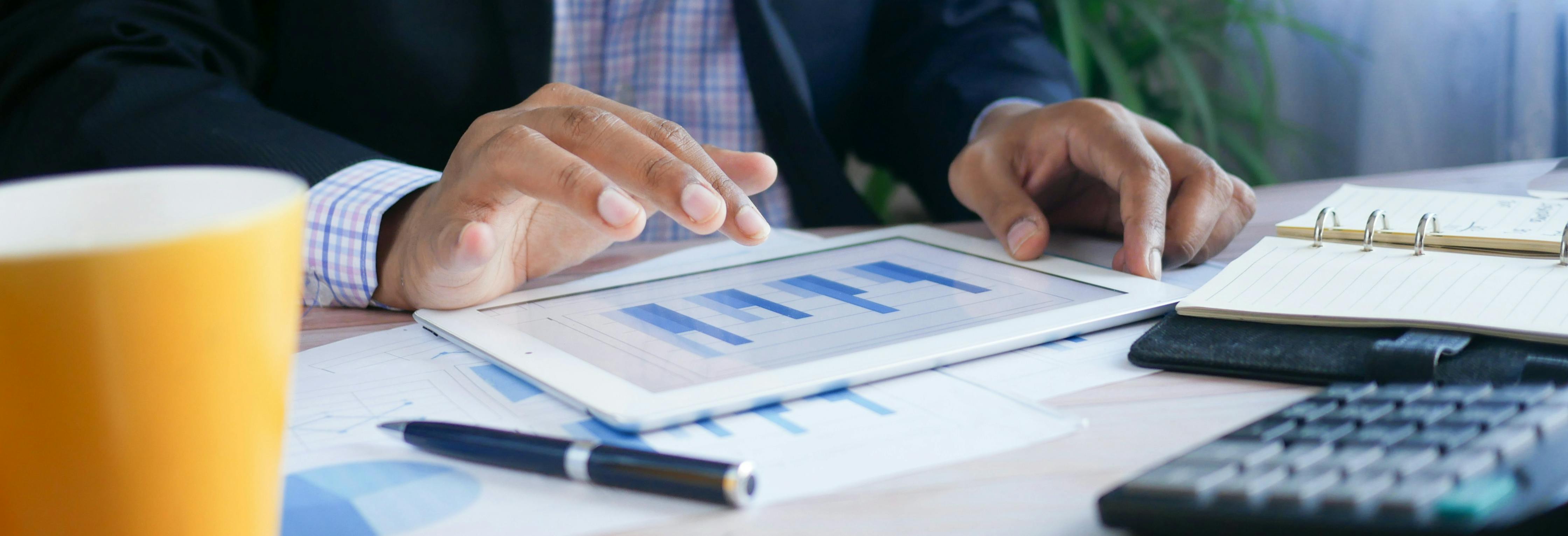 Person at a desk working on a tablet with graphs and data