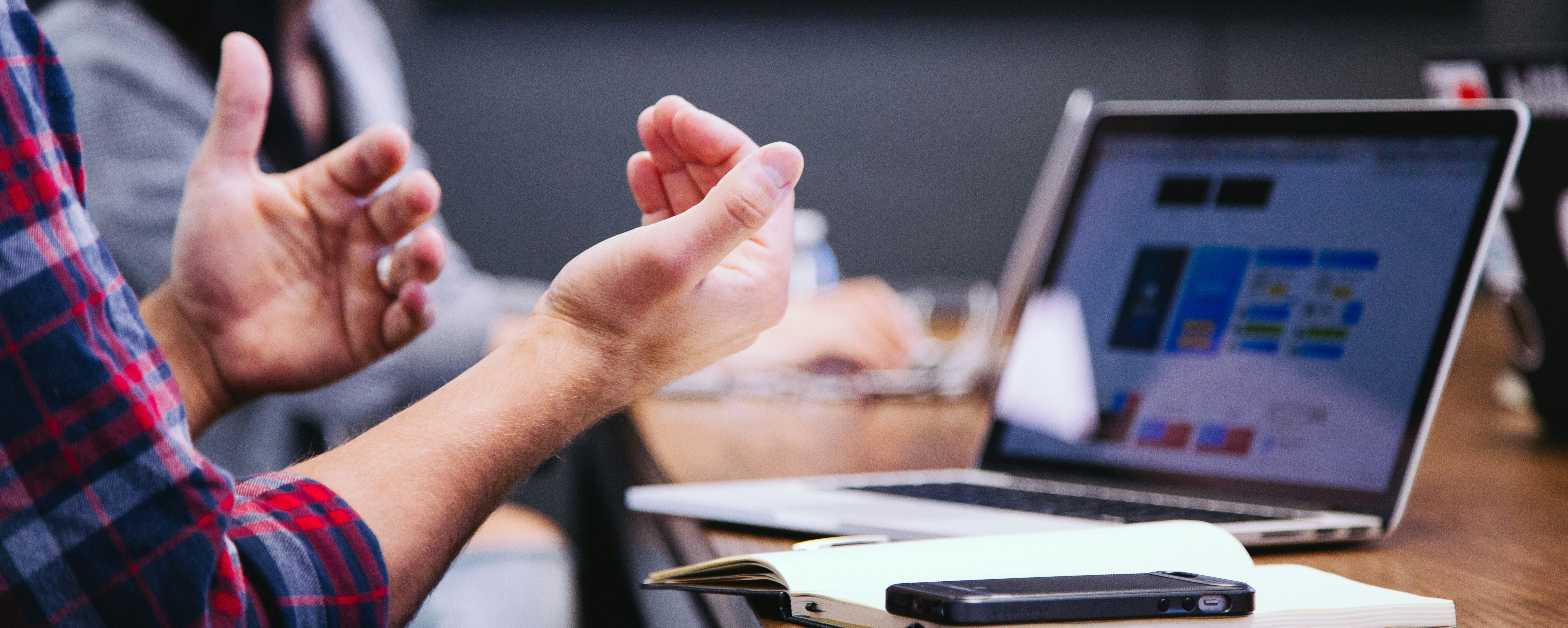 Person at a conference table motioning with their hands and in front of an open laptop