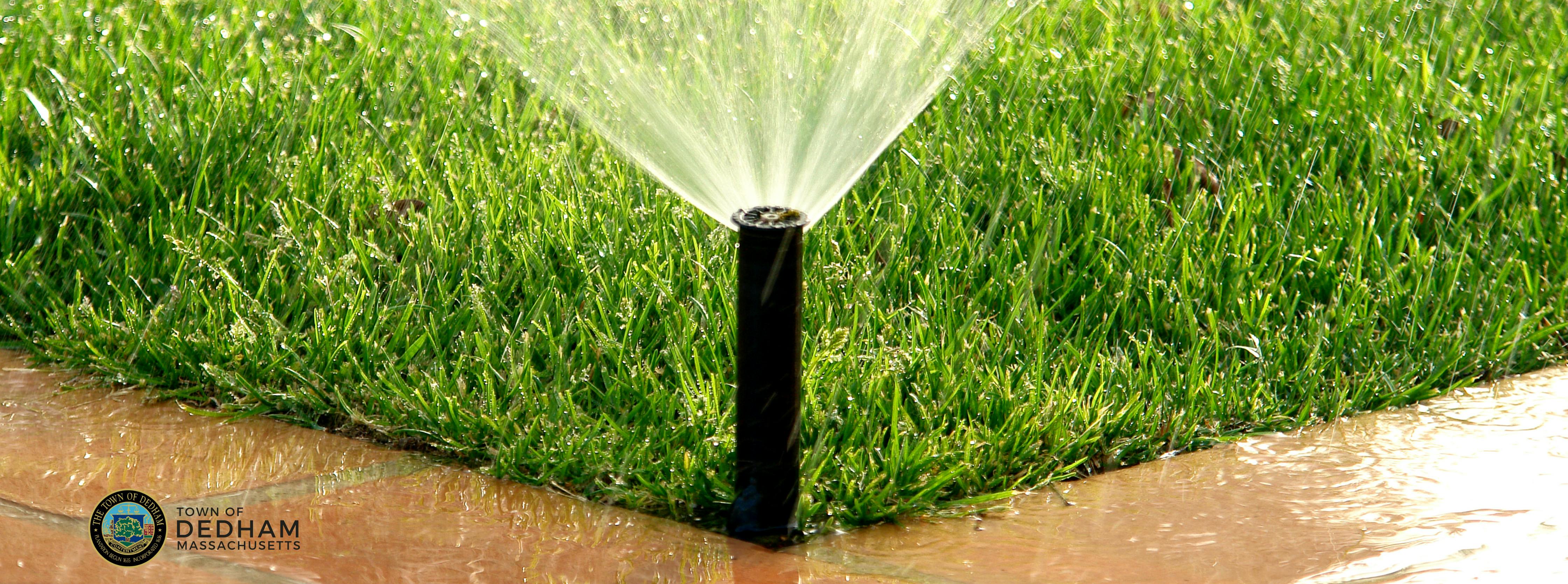 sprinkler spraying water on grass near corner of walkway