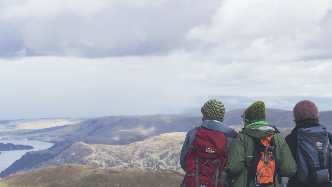Three people with backpacks stand at the top of a mountain range looking at the state park