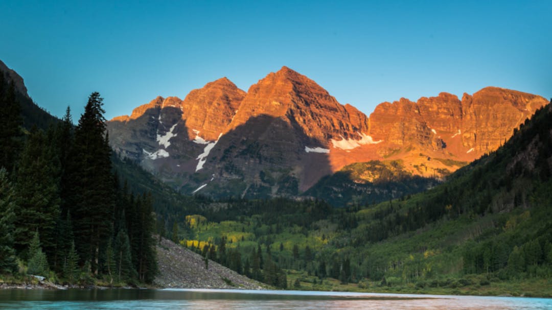 The Maroon Bells range highlighted by sunlight, with the lake below in shadow.
