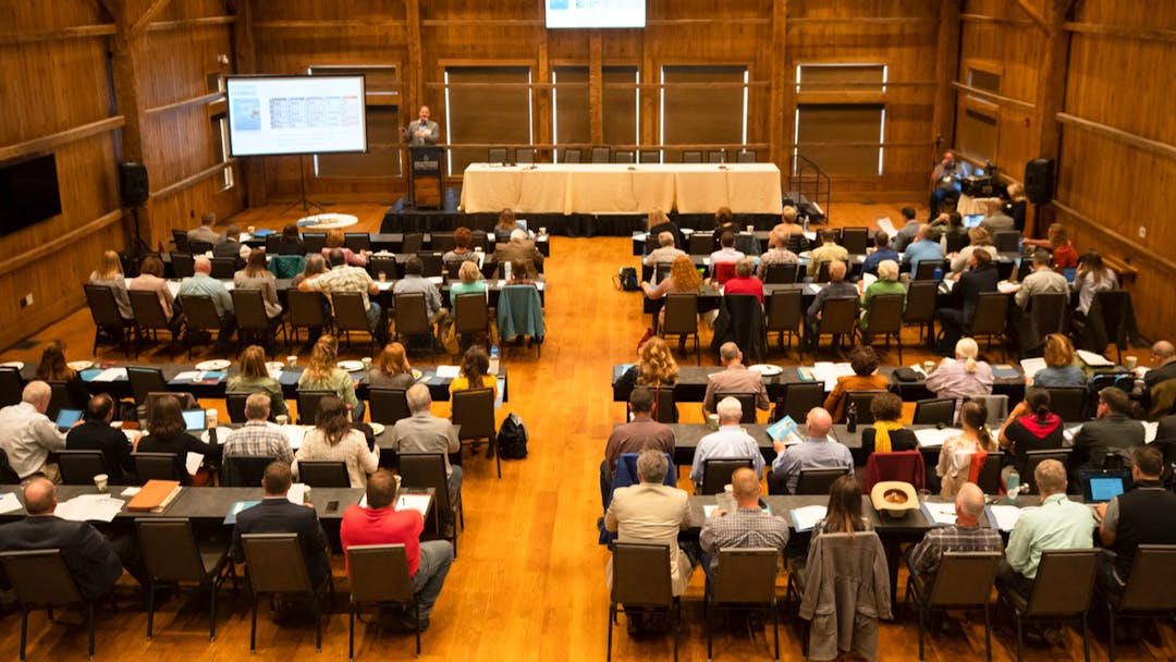 People sit in rows at a public meeting.