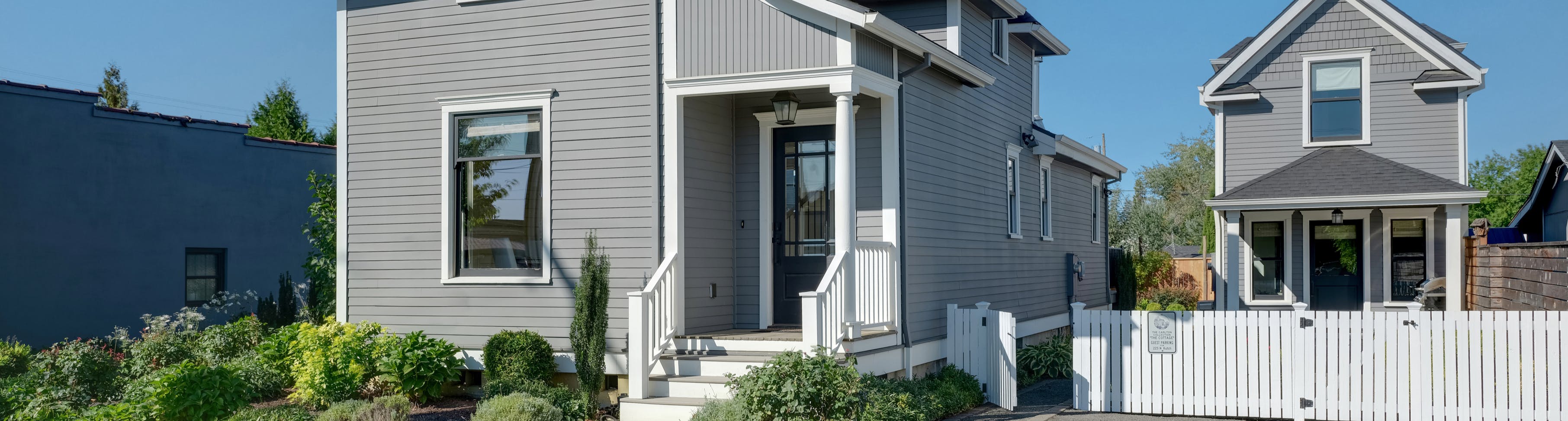 Two story blue house surrounded by green grass, sidewalks, and a driveway that leads to an accessory dwelling building.
