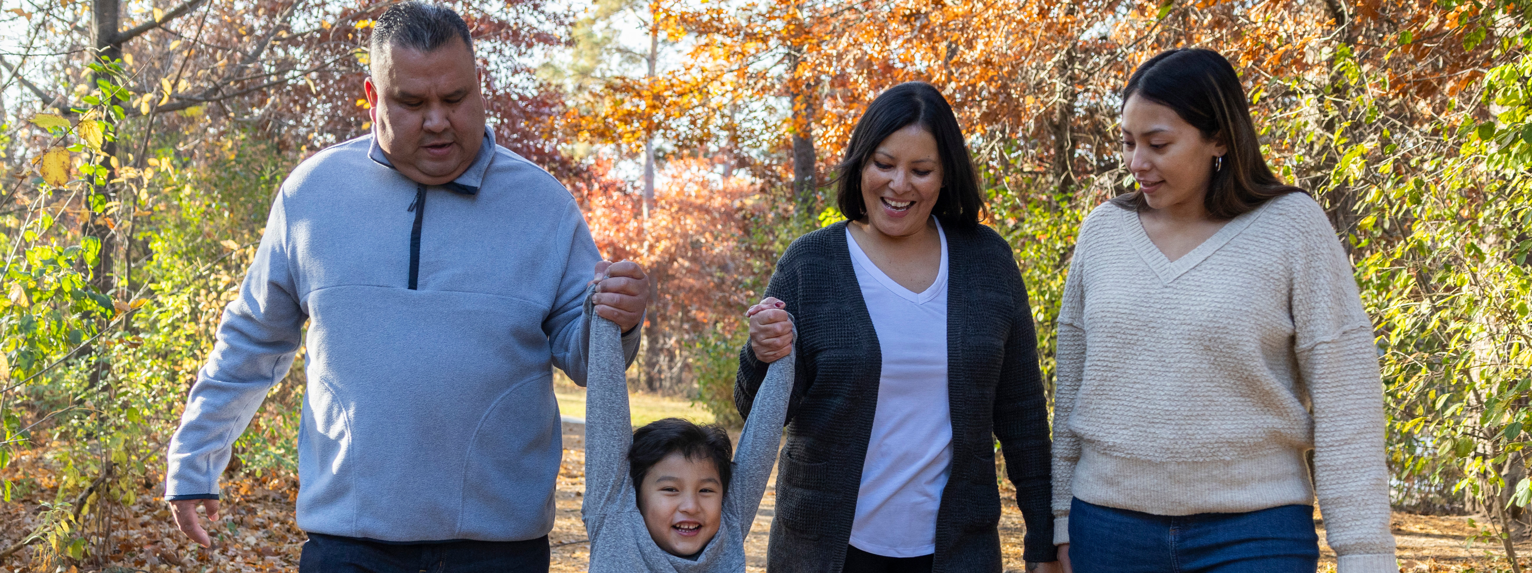 Family walking through the woods holding hand on a bright fall day. 