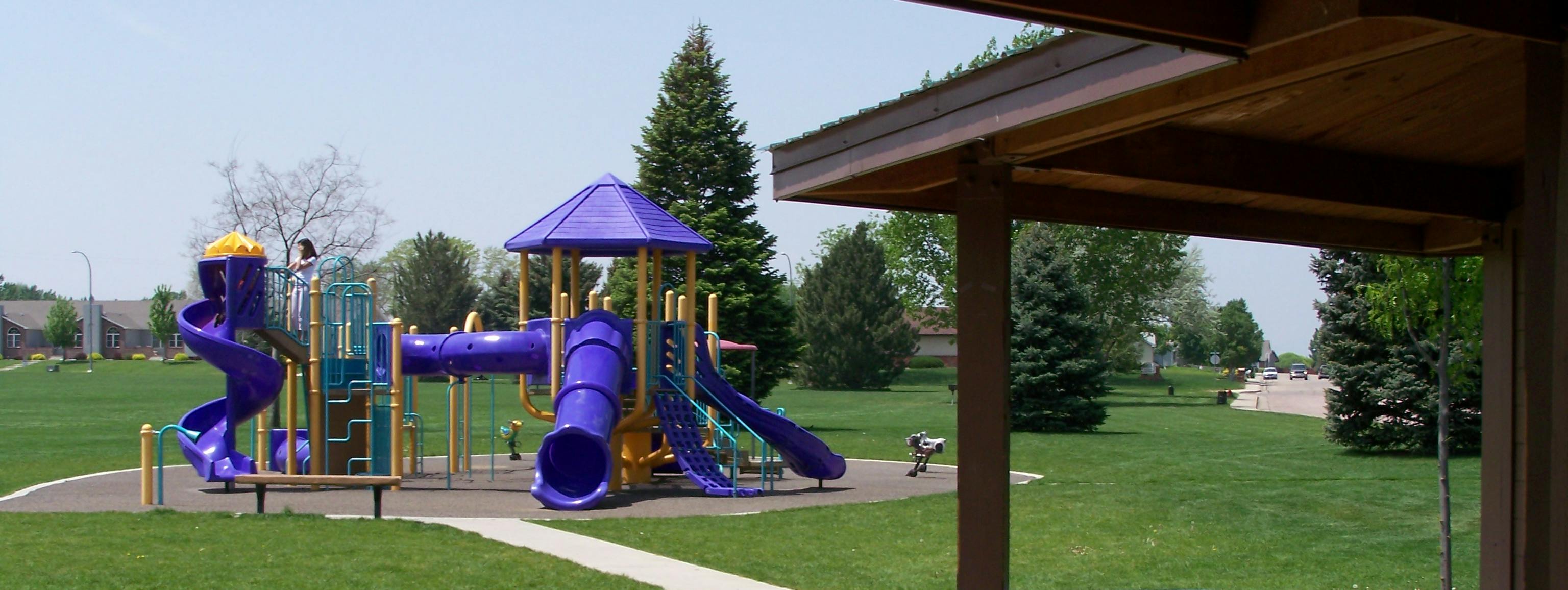 A purple playground with slides surrounded by grass in a park
