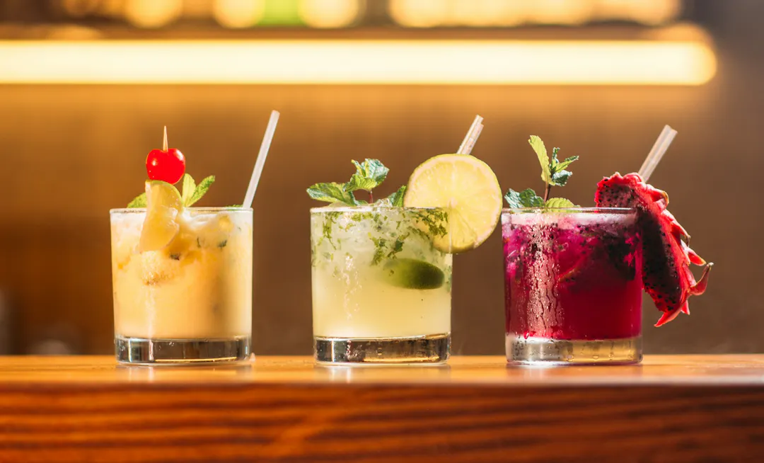 three tropical-looking cocktails in short glasses on a bartop