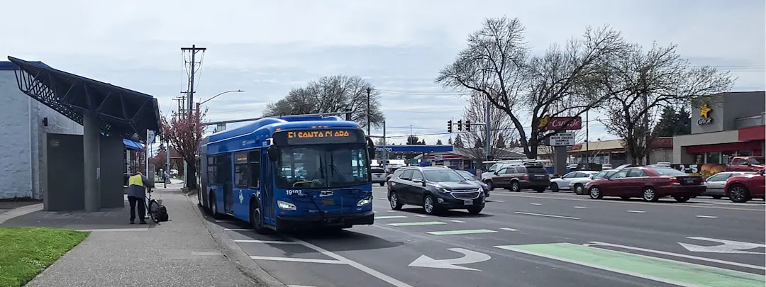 The foreground shows a blue bus driving in the left turn lane while other traffic goes both directions on River Road