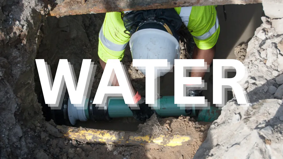 Worker repairing or installing an underground water line in a construction trench.