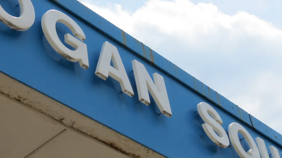 A blue 'Logan Square' sign on a building, against a partly cloudy sky.