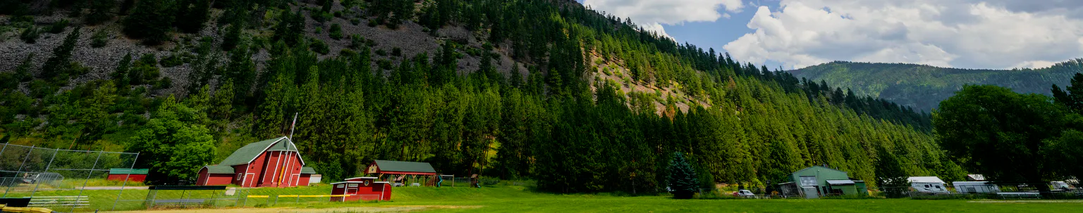 red barn in the country with the green forest in the background and blue skies