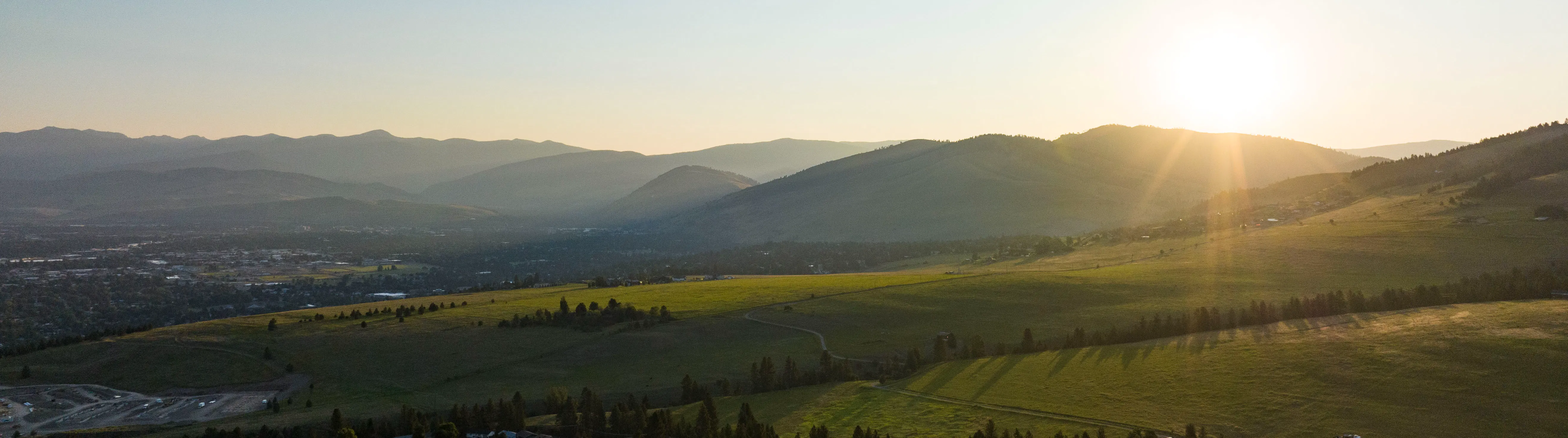 green hills with a small city in the forefront and blue skies