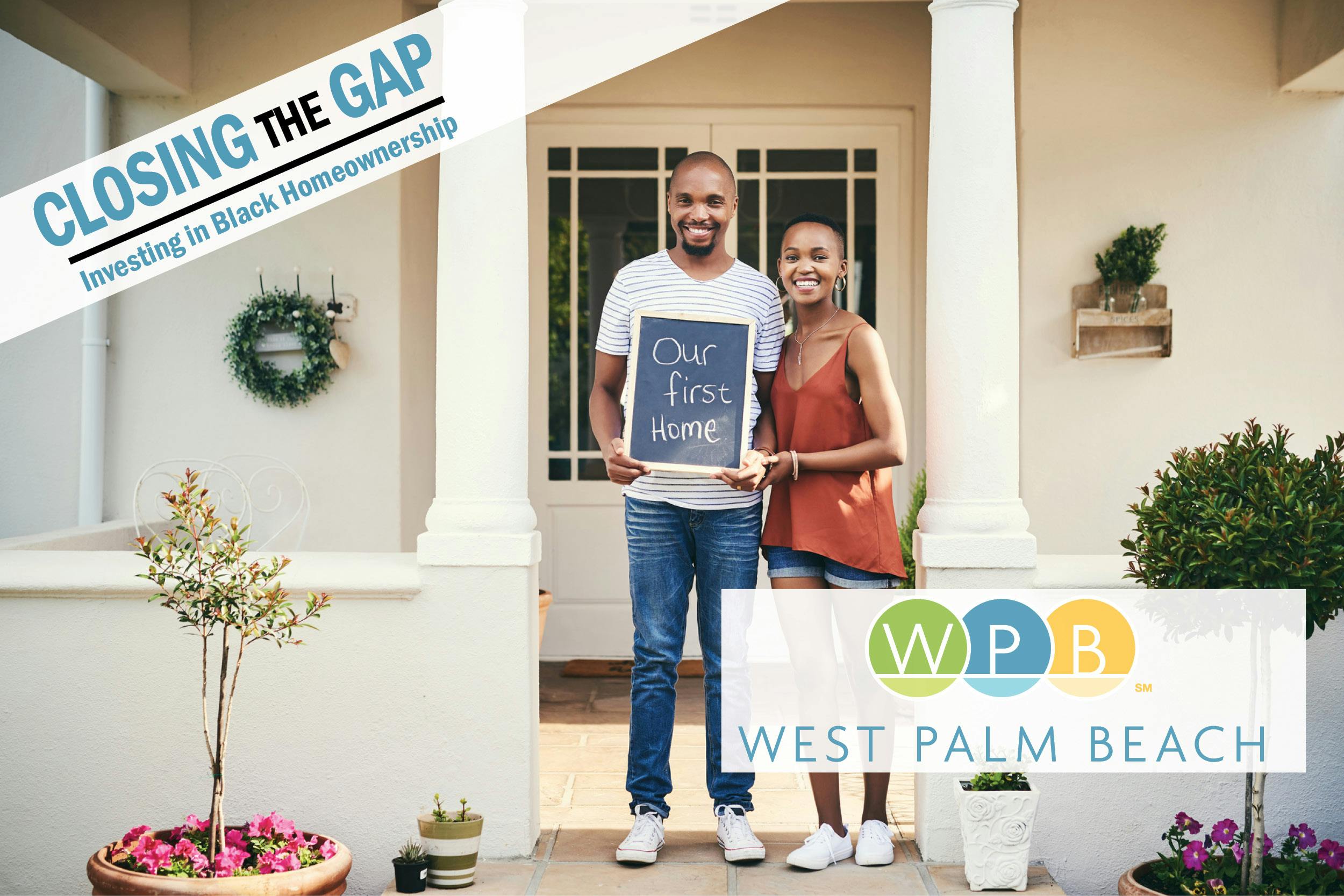 Two people who purchased a home standing on the front steps holding a sign that says "our first home".