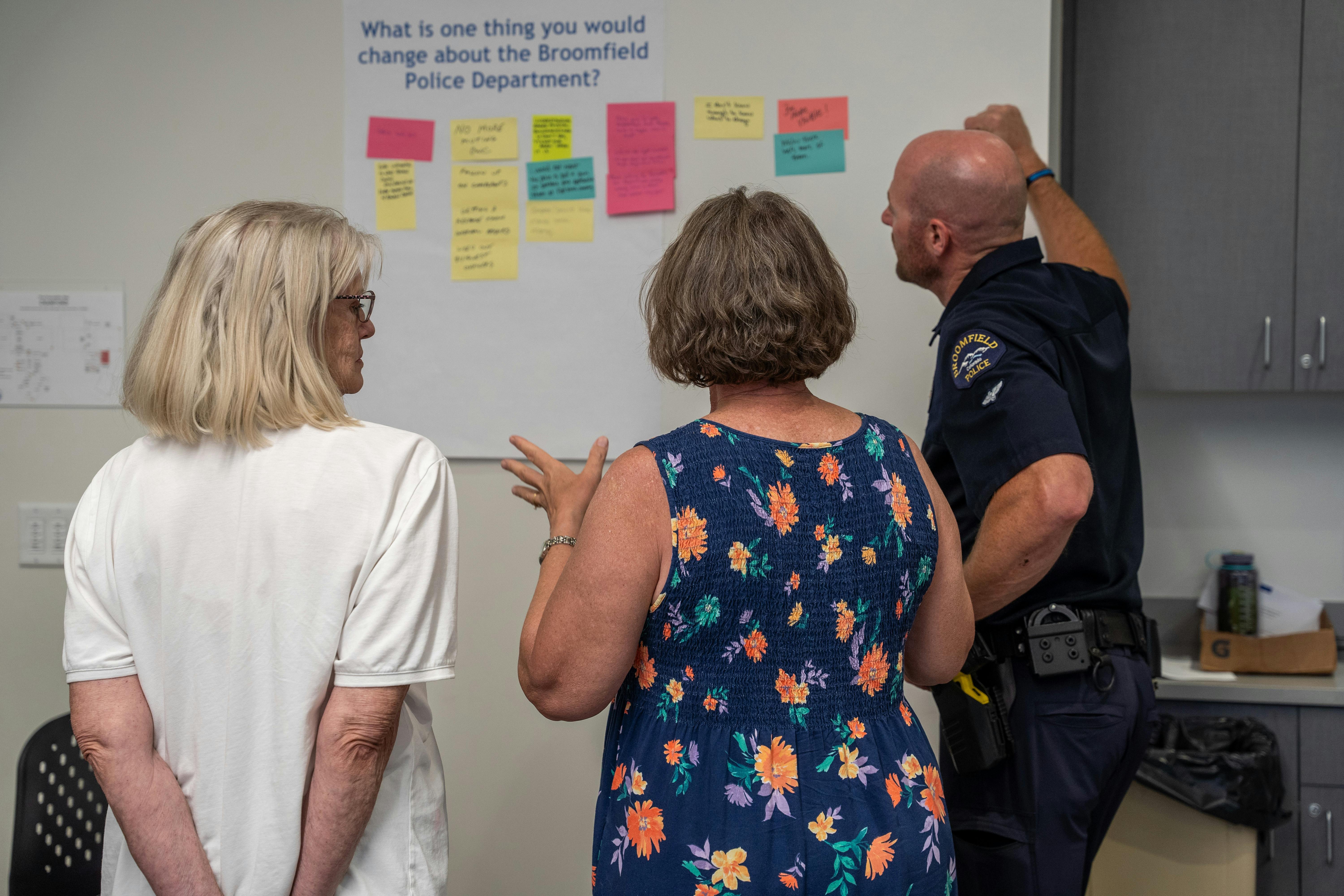 Two women stand discussing some of the sticky note comments on a poster