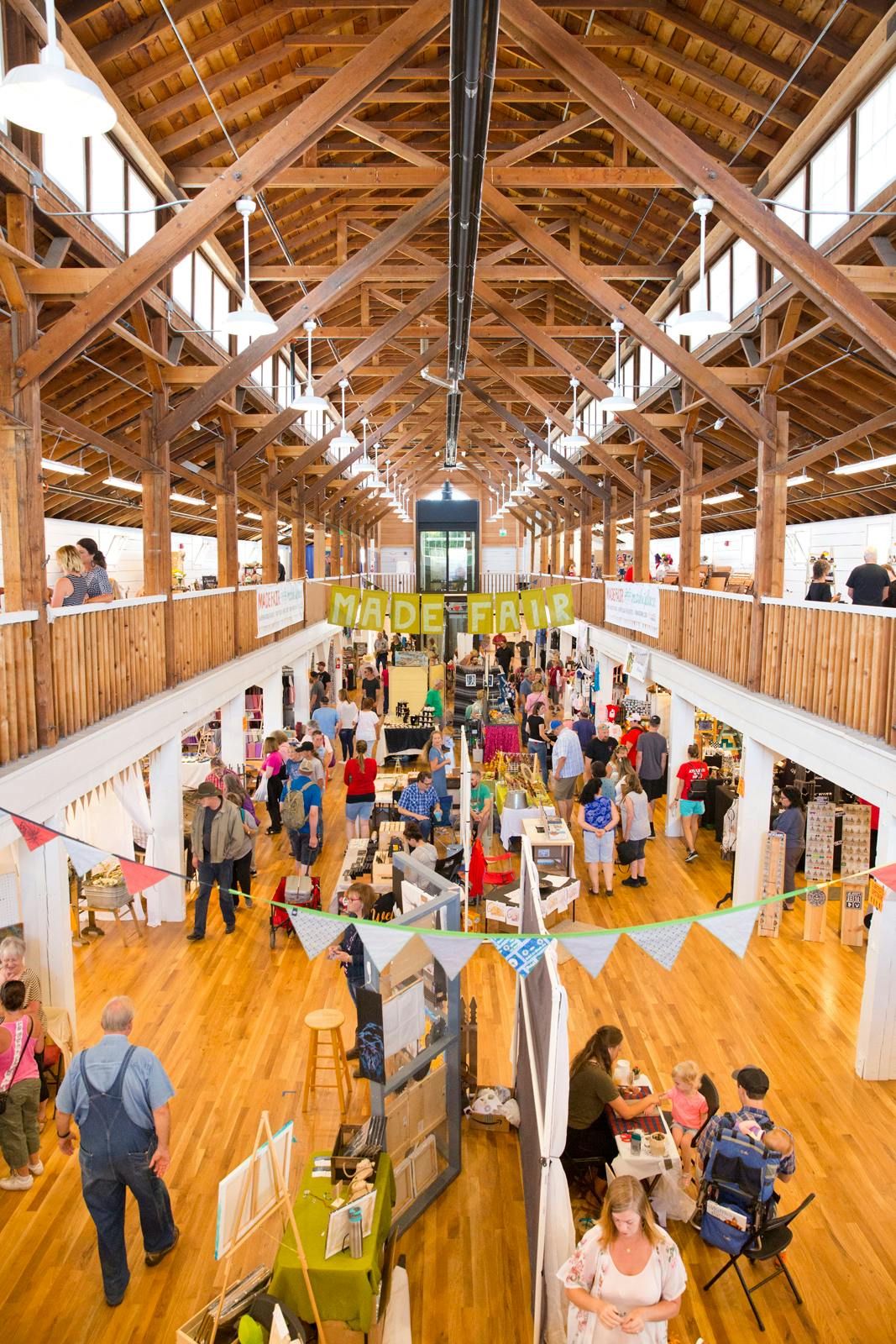 The Commercial Building on a busy day of the Made Fair. Craft vendors line the center of the room as people peruse the merchandise.